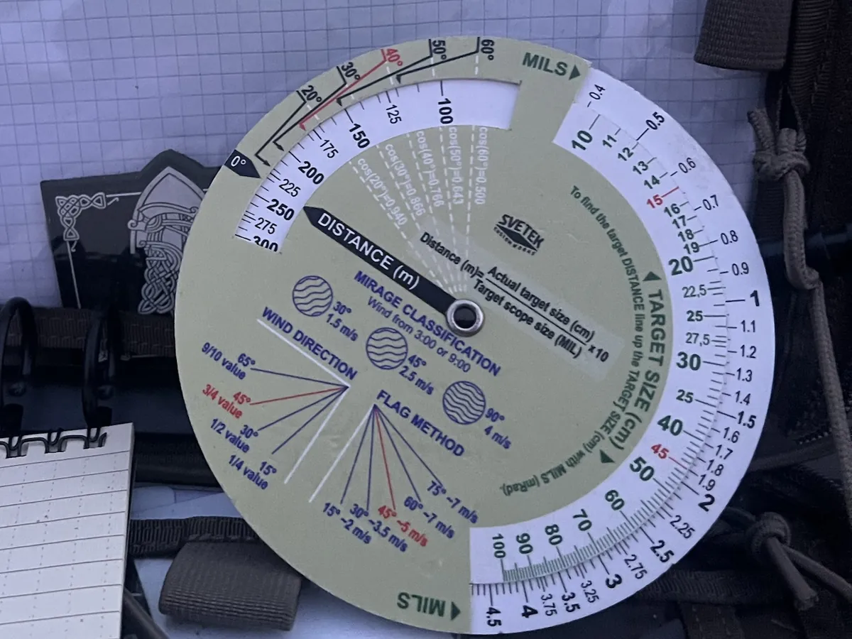 Mil-ranging disc in an admin pouch next to a notebook, scales readable at a glance